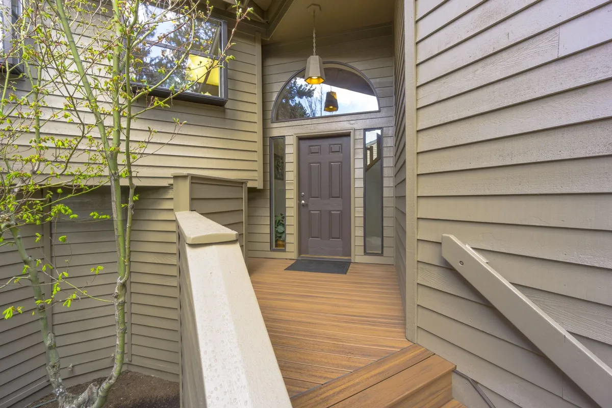 This image features the home's welcoming front door, wooden steps, hanging light fixture, and bright windows, offering a glimpse of the entryway which leads directly to the outdoors. The scene is inviting and hints at easy indoor-outdoor living, which is ideal for guests with pets eager to explore nearby trails.