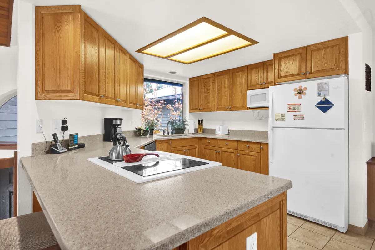 A modern kitchen with a central island, stainless steel appliances, wooden cabinets, and a large window letting in natural light. The setup is inviting and functional, ideal for cooking and socializing, with space for family gatherings and entertaining guests.