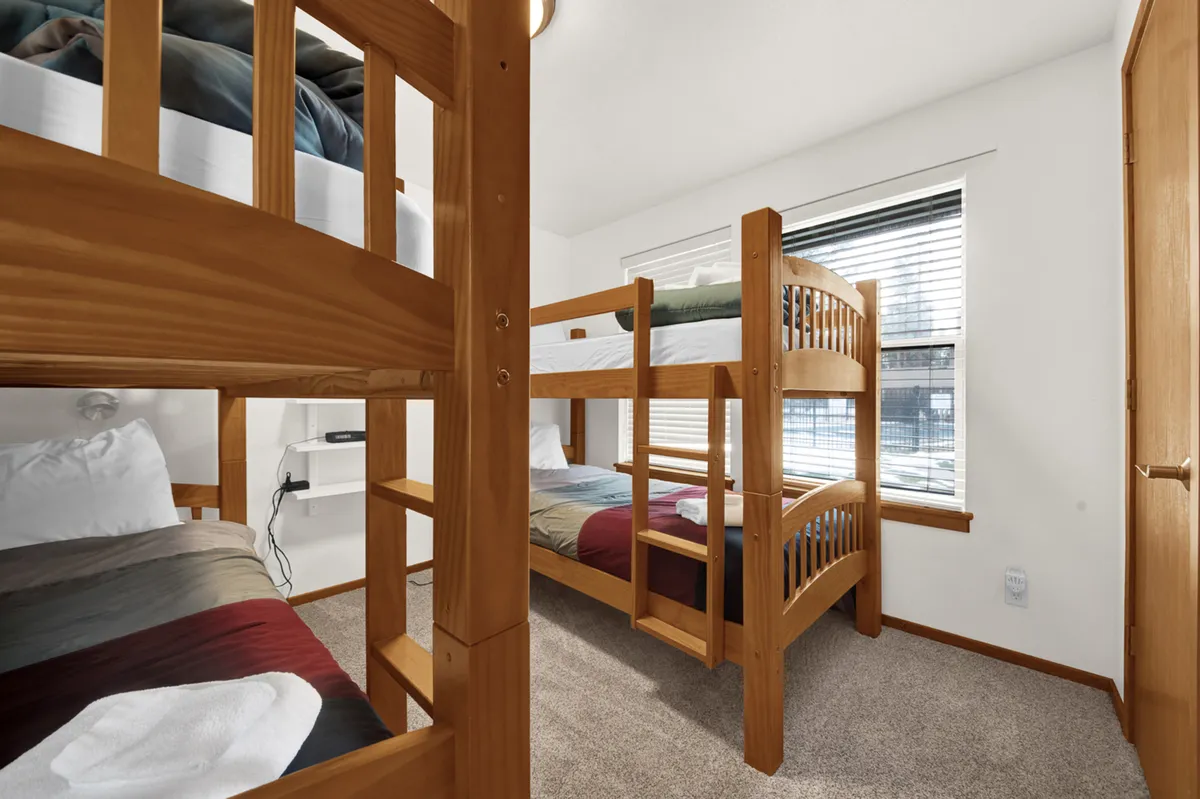A cheerful bunk room with comfortable bunk beds, playful bedding, and plenty of natural light streaming through a window. The space is inviting and ideal for children, evoking a sense of fun and relaxation.