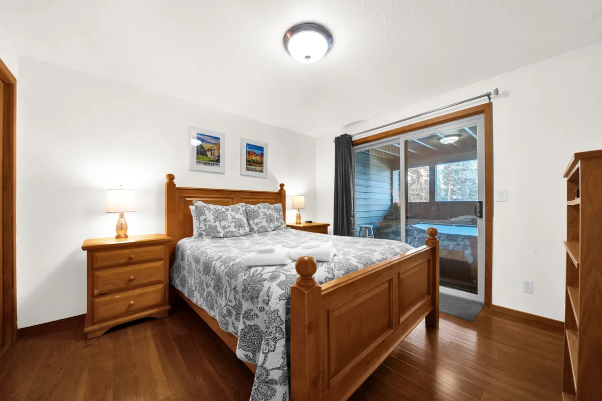 A cozy bedroom with patterned bedding, wooden furniture, and a sliding door that opens directly to an outdoor area. The natural light and view through the sliding door suggest an easy transition from restful indoor spaces to outdoor exploration.