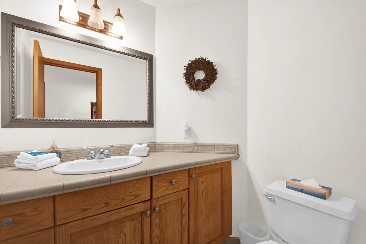 This tranquil bathroom scene highlights a stylish vanity with a decorative mirror, fresh plush towels, and a calming wreath. The area looks inviting and thoughtfully prepared for self-care and everyday comfort.
