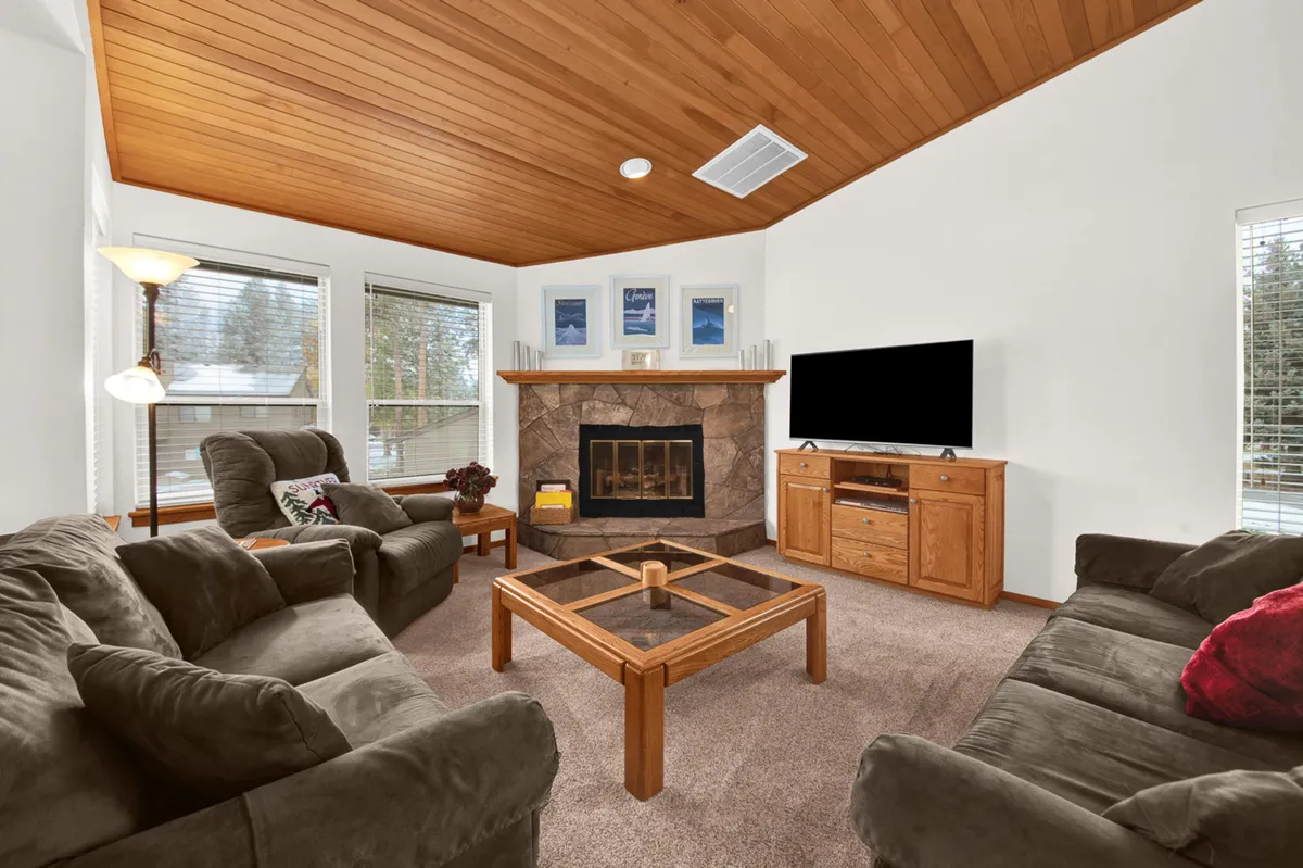 A cozy living room is depicted, with a central fireplace, comfortable sofa, coffee table, and TV. The setup is inviting, ideal for gathering with loved ones, enjoying warm drinks, and having cozy nights indoors by the fire.