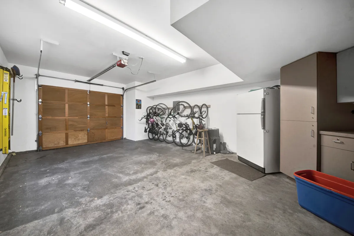A practical garage space featuring bicycles mounted on the wall and organized storage, with a refrigerator and red storage bin nearby. The setup suggests ready access to bikes for outdoor adventures and family rides.