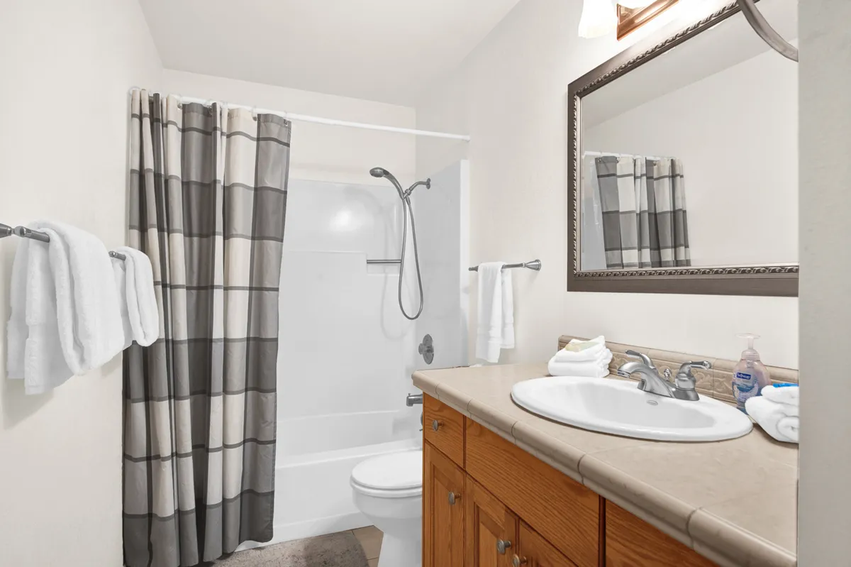 A practical and inviting bathroom featuring a modern sink with countertop, a shower area, a large mirror, and neatly organized towels. The atmosphere is clean and refreshing.